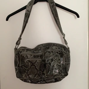 Väska från Nuunoo - Väska i lite större modell från Nuunoo. Ormskinnsmönster🙌 Använd fåtal gånger så är i bra skick. Finns extra band till. Köpt på Nelly för cirka ett år sedan för cirka 1000kr. Köparen står för frakten🥰 Pris: 300kr