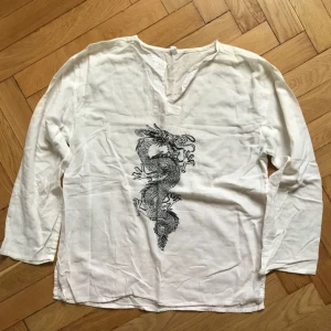  - Vit linne-aktig skjorta/blus med drake på i 90-tals-stuk. Någon enstaka skavank. S/M - på mig som är XS blir den lite lagom luftig och lätt ”oversize”.