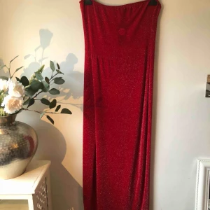 - Röd glitter långklänning utan axelband, har en hög slotts på höger sida. Aldrig använd o prislappen sitter kvar. 