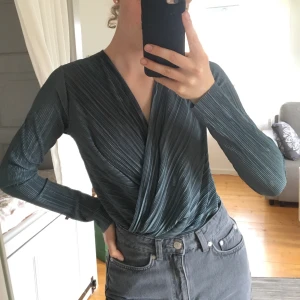 Omlott body - Helt oanvänd body från Gina tricot. Har ett väldigt skönt och ”vågigt” material i en fin grönaktig färg. Frakt på 40kr tillkommer och betalas via swish. 