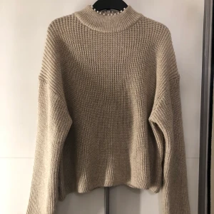 Stickad tröja med pärldetaljer - En beige stickad tröja från H&M med pärlor på kragen, storlek S. Använd endast en gång och har inga fel. 