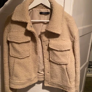 Teddy Jacka - Beiga jacka i teddymaterial och kort modell. Använd under 1 vinter. Storlek: 36. Kostaden är 150kr + frakt