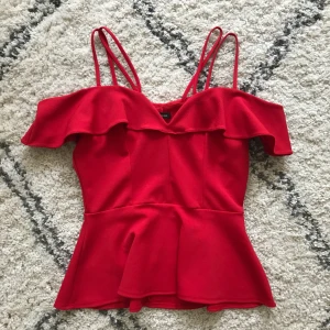  - Snygg topp med två band som går över axlarna och ”open shoulder” detalj med volang hängandes på armarna. Endast använd 1 gång, så säljes i nyskick. Köptes för 400-500kr