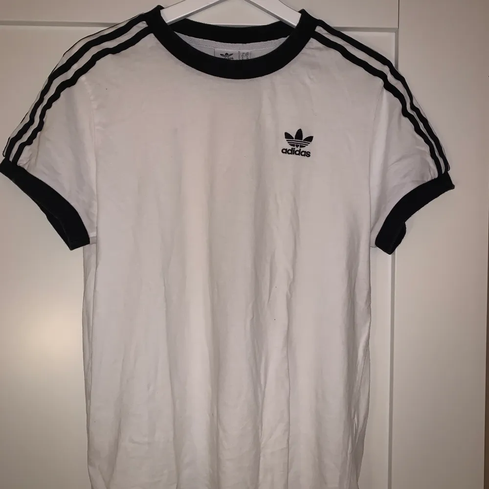 Adidas t-shirt med tre streck på ärmarna och konstrast i alla ändar. I bra skick. Nypris 299kr, säljs för 100kr. Strl 36 ifrån Adidas🖤. T-shirts.