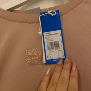 Adidas  - Adidas Crew Sweatshirt. Aldrig använd. Den ska vara Oversized. Den är lite mer åt det rosa hållet men är ändå beige. Glitter på märket och lite glitter på dem 3 sträcken med. Priset och frakten kan diskuteras. 