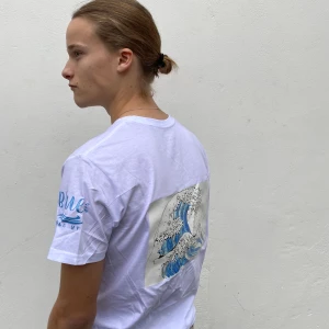 Blue Rescue UF HERR - Storlek: S-L. En vit stilren t-shirt med ett tryck föreställande havet på tröjans baksida 🌊 20% av vinsten går till WWF 🌍💙