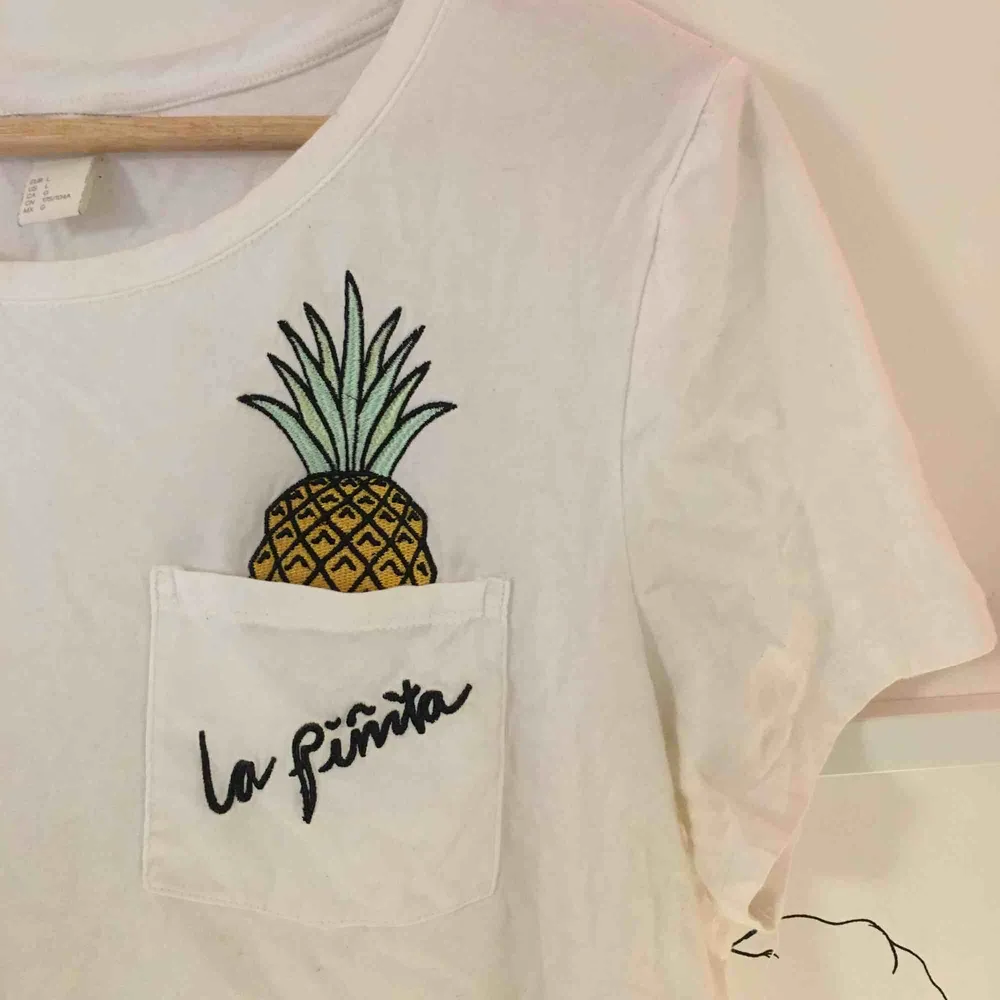 Jätteskön vit t-shirt från H&M med en charmig ananas som sticker upp ur bröstfickan🍍. T-shirts.