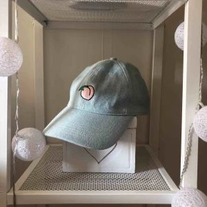  - Cool keps med 🍑 tryckt på från Pull&Bear. Kepsen är gjord av jeans material och har ett gulligt tryck pp baksidan som citerar, ”Shake your peach”. Kepsen går att spänna på baksidan.