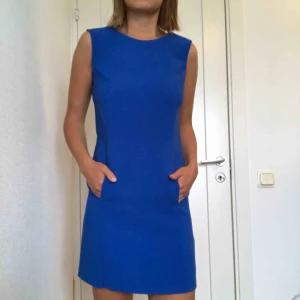  - Blå fin klämning med genomgående ficka på magen. Liten ”spricka” längst mer på ena sömmen på klänningen men som lätt går att sy ihop.