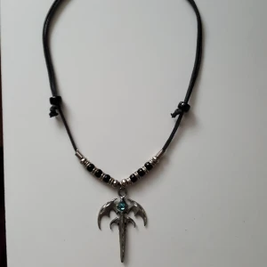  - Halsband med svart snöre och hänge i, vad jag tror är, metall med en blå sten/kula. Fraktkostnad blir 11kr.