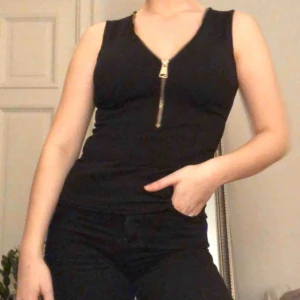  - Svart linne med guldig dragkedja som man själv kan bestämma urringningen på. Helt oanvänd. Köparen står för frakt:)