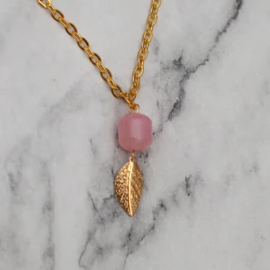 Halsband löv  - Halsband med rosa glaspärla och guldfärgat löv. Hänget är ca 2,5cm. Kedjan är ca 60cm. Obs! Den är inte orange som på bilden, Photoshop ändrar färgerna för mig 🙃 11:- i frakt, fri frakt vid köp över 100:-.