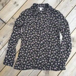  - Blus i chiffong svart botten med små söta blommor. Liten frill udd på rundad krage. Så snygg enkel till denim. 