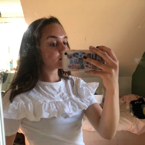 Vit t-shirt med cool volang detalj - En vit, simpel tröja med en snygg volang detalj vid bröstet. Startpris = 60kr