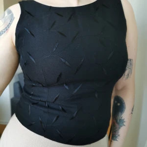 Broderad topp  - Topp med svart broderat växtmönster. Dragkedja bak. Uppskattningsvis strl S (står 7/8 på lappen) Byst 94 cm, längd 40 cm. Köparen står för porto 55 kr. 