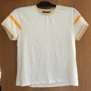 Vit t-shirt med gula detaljer - Stretchig vit tröja med gula detaljer. I storlek L, men skulle nog passa någon i storlek M då den sitter lite tight på mig. Köpare står för frakt.