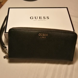 Guess plånbok - Äkta Guess väska som endast använts enstaka gånger, mycket bra skick! Inköpt för 649kr från Åhléns men säljer för bara 350kr. Model: Pin Up Pop Slg Zip