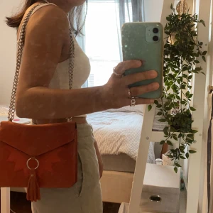Orange väska  - Cool somrig kedjaväska från märket ICHI. Den är i en orange mocka färg och går ner till höften. Kostar 200, frakten ingår inte 