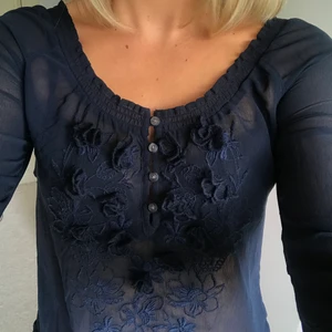 Mörkblå blus - Vacker mörkblå blus med rund urringning. Fina detaljer, knappar och blommor. Väldigt bra skick. Köparen står för frakt😊