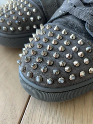Gråa sneakers med nitar - Unika grå sneakers i mocka med massor av silvriga nitar och spikes över hela skon. Tjock sula och klassisk snörning framtill. Perfekta för dig som vill sticka ut och addera edge till din stil.
