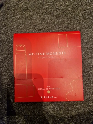 Rituals Me-Time Moments presentkit - Lyxigt presentkit från Rituals i serien The Ritual of Ayurveda. Innehåller fyra produkter för kropp och ansikte, bland annat foaming shower gel och face & body clay mask. Förpackningen är röd med gulddetaljer och har en elegant design. Perfekt för egenvård och avkoppling.