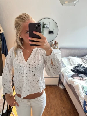 Vit broderad blus med v-ringning - Säljer en superfin vit blus med broderade hålmönster och v-ringning. Blusen har långa ärmar med resår vid handlederna och en avslappnad passform. Perfekt till jeans eller kjol för en fräsch look. Materialet känns lätt och luftigt.