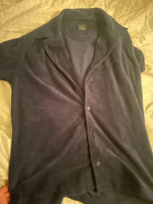 Mörkblå frottéskjorta från Jack and Jones - Kortärmad skjorta i mörkblå frotté. Skjortan har klassisk krage, knappar framtill och en mjuk känsla. Perfekt för en avslappnad och trendig look.