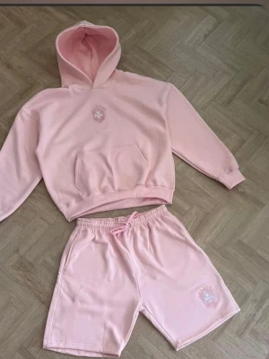  Brasiliansk Ljusrosa hoodie och shorts set - Säljer ett ljusrosa set med hoodie och shorts. Hoodien har magficka och broderad logga på bröstet, medan shortsen har resårmidja med snöre och matchande broderad logga. Mjukt och bekvämt material, perfekt för en avslappnad look. DE FINNS I ALLA STORLEKAR!!!