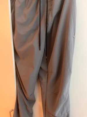 Grå mjukisbyxor med dragsko - Snygga grå mjukisbyxor med avslappnad passform och svarta dragsnören i midjan. Tillverkade i ett mjukt och bekvämt material som passar perfekt för chill dagar. Byxorna har raka ben och enkel design utan synliga loggor.