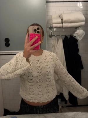 Vit virkad stickad tröja - Säljer en vit stickad tröja med virkat mönster och rund hals. Tröjan har långa ärmar och vågig kant nedtill, vilket ger en söt och trendig look. Perfekt för dig som gillar en avslappnad men ändå stilsäker outfit.