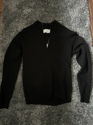 Svart halvzip-tröja från Norvie - Snygg svart långärmad tröja från Norvie med halvzip och hög krage. Tröjan har en minimalistisk design och är tillverkad i ett mjukt material som passar perfekt till många olika stilar. Aldrig använd.