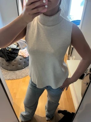 Beige Zara  polotröja - Säljer en beige ärmlös polotröja i mjukt stickat material. Tröjan har hög polokrage och en avslappnad passform som ger en snygg siluett. Perfekt att styla med jeans eller kjol för en trendig look.