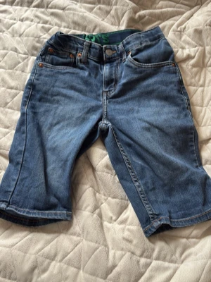 Blå jeansshorts från Levi's - Klassiska blå jeansshorts från Levi's med fem fickor och knappgylf. Shorts i normal passform med raka ben och typisk Levi's-lapp bak i midjan. Perfekta för en avslappnad stil och tillverkade i slitstark bomull.
