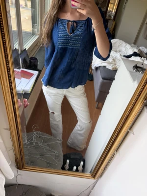 Marinblå blus med broderi och knyt💗 - Säljer en marinblå blus med broderade detaljer och knyt framtill. Blusen har trekvartsärm och en lös, flowy passform. Perfekt till jeans eller kjol för en avslappnad men snygg look!!