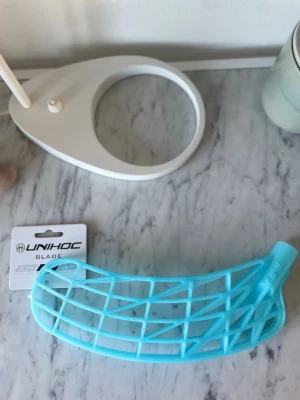 Blått innebandyblad från Unihoc - Säljer ett ljusblått innebandyblad från Unihoc. Bladet har ett öppet rutmönster och är tillverkat i plast. Perfekt för dig som vill byta blad på din klubba och få bättre bollkontroll.