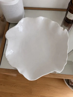 Vit dekorativ keramikskål - Säljer en vit keramikskål med organisk, vågig form. Skålen har en blank yta och unik design som gör den till ett snyggt inslag i hemmet, perfekt för dekoration eller servering. Passar bra på soffbordet eller som fruktfat. Stora storleken