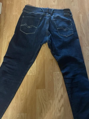 Mörkblå jeans från Replay - Säljer ett par mörkblå jeans från Replay med klassisk femficksdesign och snygga kontrastsömmar på bakfickorna. Jeansen har rak passform och är tillverkade i slitstarkt denim-material. Perfekt för dig som gillar en tidlös och clean look. Använt få gånger. Nypris 1200kr, Storlek 34