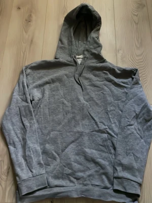 Grå hoodie från Pier One - Säljer en enkel och stilren grå hoodie från Pier One. Hoodien har huva med dragsnören och en stor magficka framtill. Materialet är mjukt och bekvämt, perfekt för chill dagar. Passar dig som gillar klassiska och neutrala plagg.