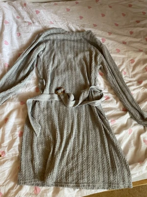 Ljusgrå stickad klänning - Mysig ljusgrå klänning i stickat material med bälte i midjan. Långärmad modell med kabelstickat mönster som ger en avslappnad och trendig look. Perfekt för unika sommarkvällar mm. Aldrig använd! Från Dubai. Säljer den eftersom den var för stor på mig:(