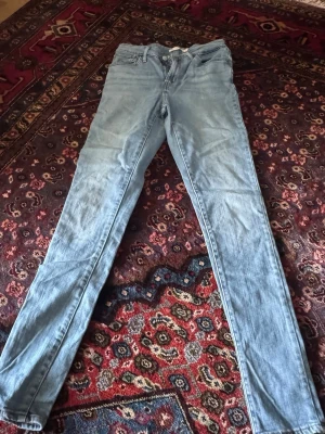 Ljusblå smala jeans från Levi's - Säljer ett par ljusblå skinny jeans från Levi's med klassisk femficksdesign och Levi's ikoniska röda etikett på bakfickan. Jeansen har normal midja och är tillverkade i mjukt denimtyg som ger en bekväm passform.