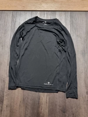 Svart långärmad träningströja Ronhill - INSTABOX!!! Svart långärmad träningströja från Ronhill. Tillverkad i ett lätt och stretchigt funktionsmaterial som andas bra, perfekt för löpning eller annan träning. Diskret logga framtill nedtill. Enkel och stilren design med rund hals.