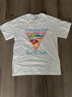 Casablanca Tennis Club t-shirt - Vit t-shirt från Casablanca med färgglatt grafiskt tryck och texten 'Casablanca Tennis Club' på bröstet. Klassisk passform med rund hals och korta ärmar. Perfekt för dig som gillar unika prints och sportig stil.