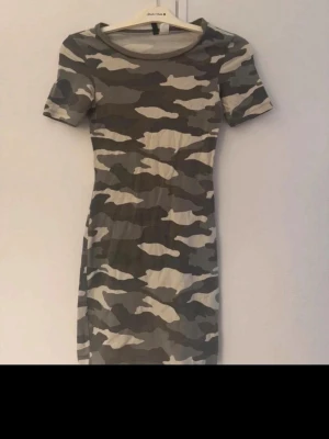 Kort camouflagemönstrad klänning H&M - Säljer en kort camouflagemönstrad klänning från H&M i storlek 32. Klänningen har korta ärmar, rund halsringning och är gjord i mjuk bomull. Perfekt för dig som gillar streetstyle och vill sticka ut lite extra.