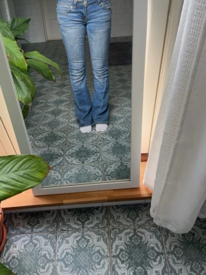 Blå bootcut jeans true religion  - Säljer ett par klassiska blå bootcut jeans från true religion med låg midja och snygga slitningar. Jeansen har fem fickor, dragkedja och knapp framtill samt en liten logga på bakfickan. Perfekta för en avslappnad och trendig look.