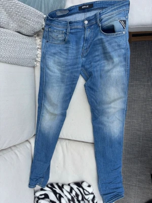 Replay jeans - Snygga blå slim fit jeans från Replay med klassisk femficksdesign och ljusa slitningar på framsidan och baksidan. Jeansen har en normal midja och är tillverkade i denim med stretch för extra komfort. Perfekt för dig som gillar en modern och avslappnad look.