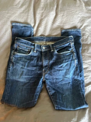 Levi's blå raka jeans - Klassiska blå jeans från Levi's med raka ben och femficksmodell. Jeansen har en snygg tvätt med slitningar och kontrastsömmar. Ikonisk läderpatch bak i midjan och röd Levi's-tag på bakfickan. Perfekta till vardagslooken.