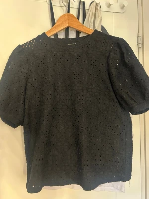 Svart spetsblus från Object XS - Svart blus från Object i storlek XS med korta puffärmar och vackert broderat spetsmönster. Blusen har rund halsringning och är tillverkad i ett lätt, luftigt material som ger en trendig och stilren look. Perfekt till vardagen med ett par jeans eller funkar lika bra till fest!