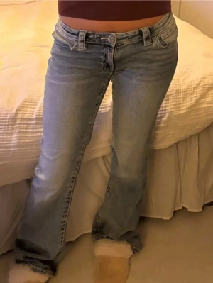 Ljusblå bootcut jeans - Säljer ett par ljusblå bootcut jeans med låg midja och klassisk femficksdesign. Jeansen har en avslappnad passform och är tillverkade i denim med lätt tvättad look. Perfekta för en casual och trendig stil.