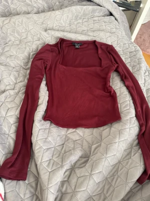 Mörkröd långärmad topp  - Säljer en mörkröd långärmad topp från med fyrkantig halsringning. Toppen är slim fit och har en enkel, stilren design utan mönster eller extra detaljer. Perfekt att matcha med jeans eller kjol för en snygg look.