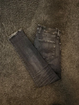 Replay anbass - Snygga mörkgråa slim fit jeans från Replay med snygg tvätt och lite slitningar. Jeansen har en mörkgrå tvätt.  Storleken är W33 L32